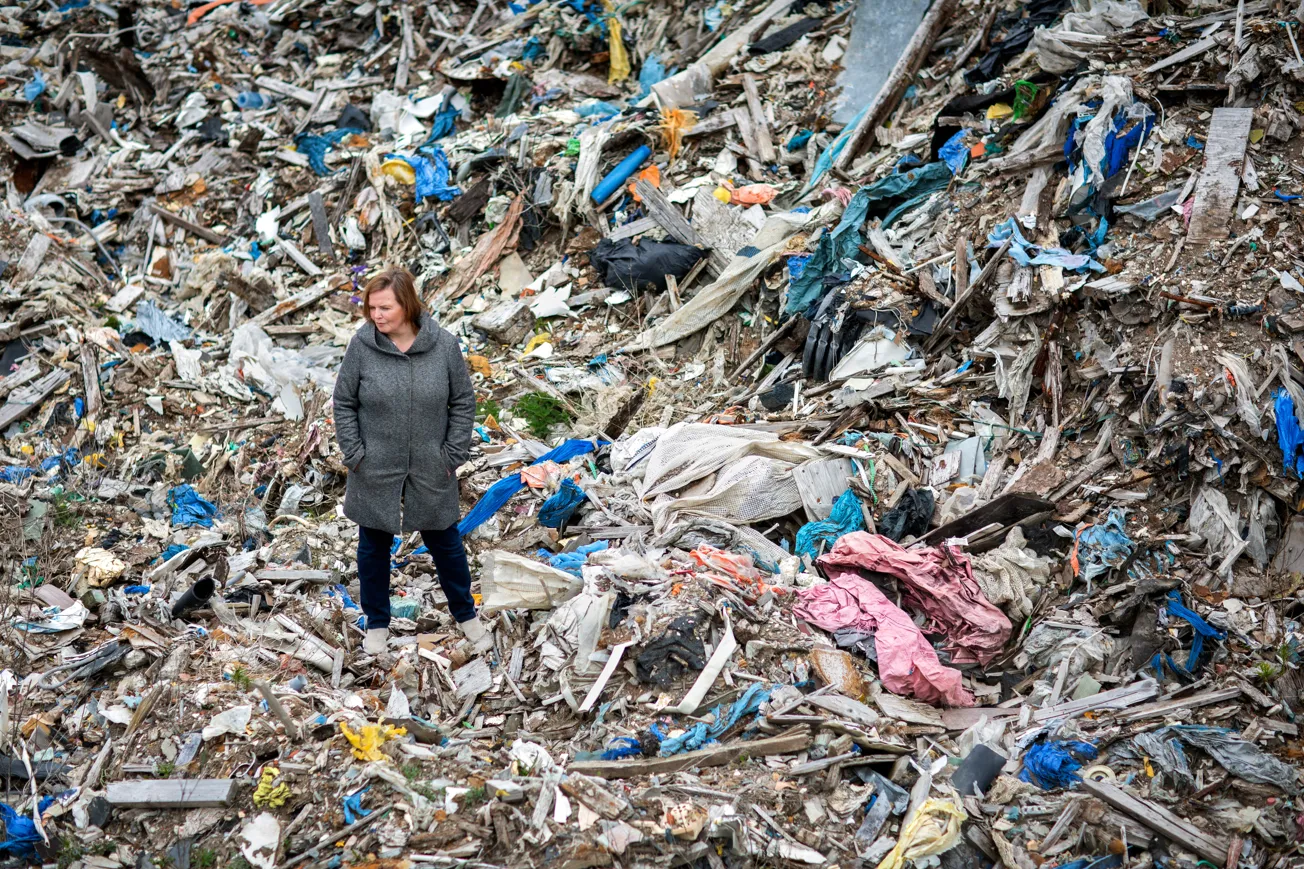 Person står bland stora mängder avfall och skräp utomhus.