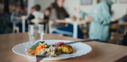 En tallrik med mat framför elever och personal som äter i en skolrestaurang.