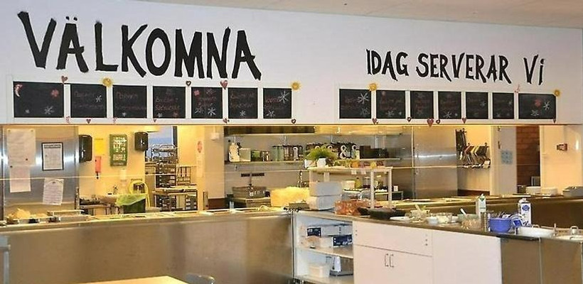 En skolrestaurang med en stor meny på väggen.