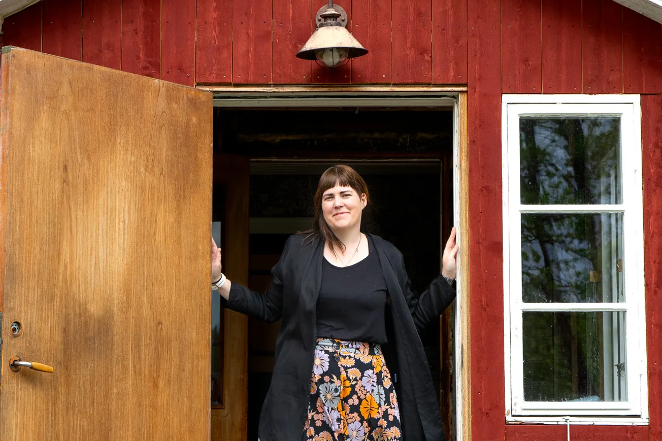 En kvinna som står i dörröppningen till ett rött hus.