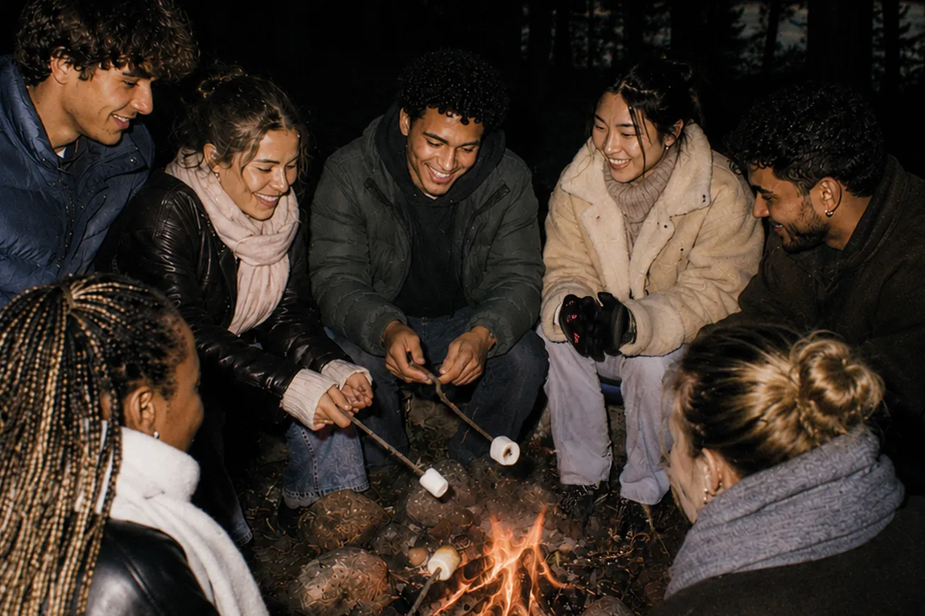 En grupp unga människor sitter framför en brasa och grillar marshmallows.