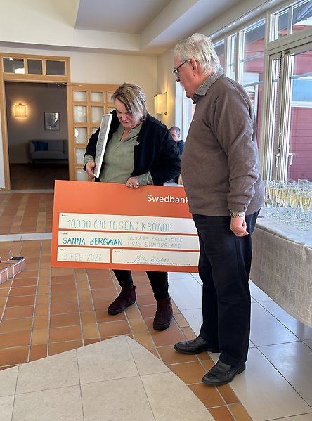 En kvinna håller i en stor papperschek med 10 000 kronor. En man står bredvid och tittar på checken.