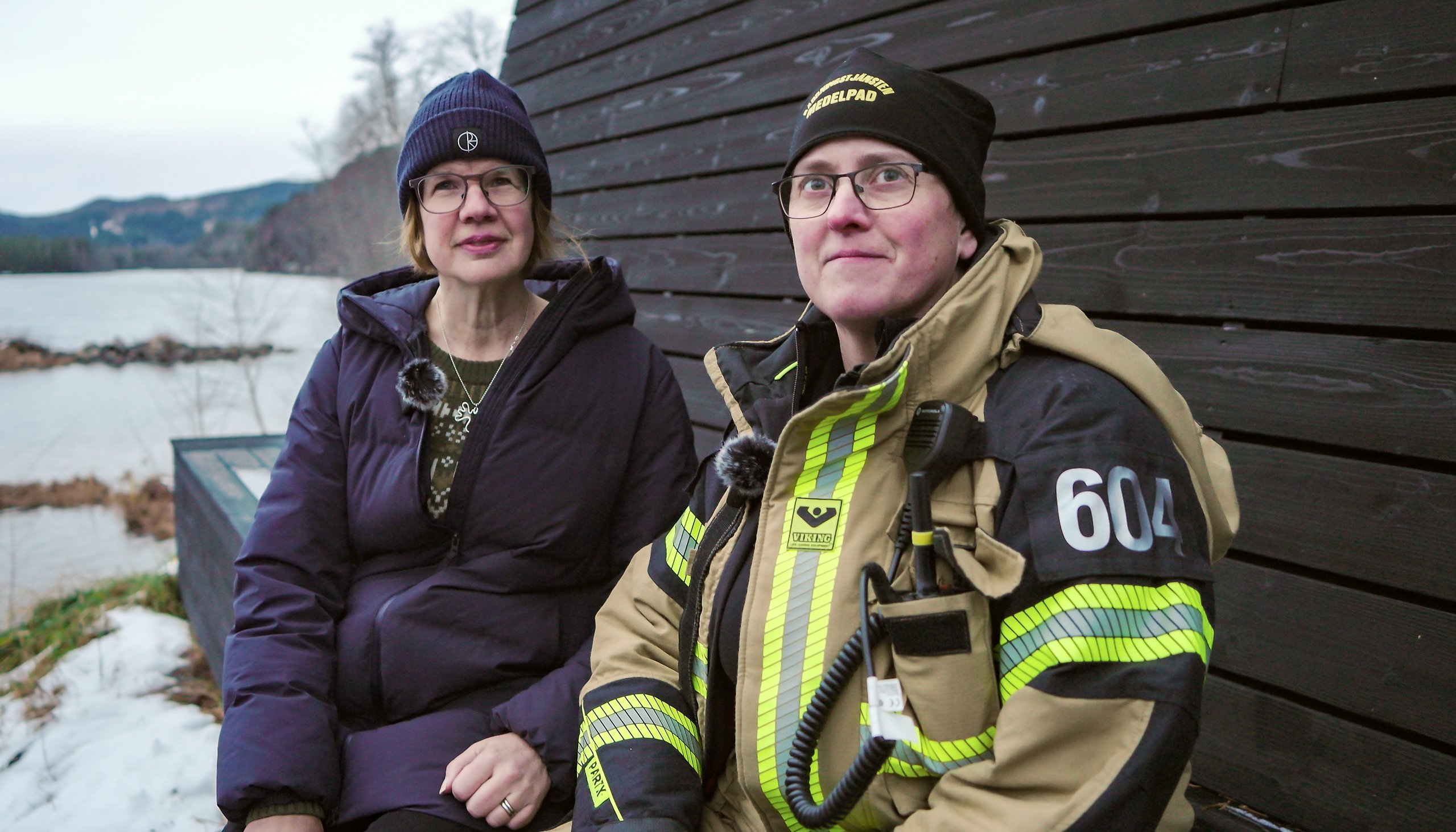 Två kvinnor sitter utomhus med en älv bakom sig