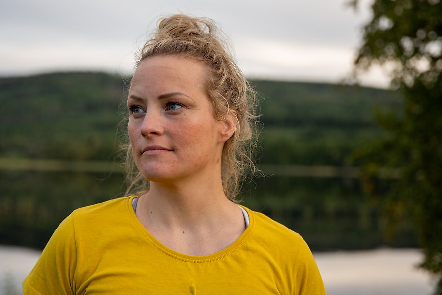 Malin Granqvist blickar ut över naturen. I bakgrunden är en sjö och en massa skog. Foto.
